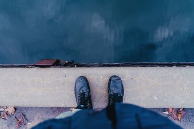 Low section of person wearing boots standing by water 