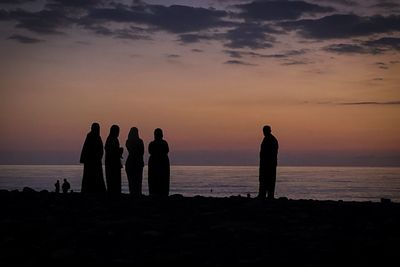 Silhouette people on beach against sky during sunset