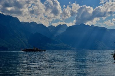 Boat sailing on sea by mountains against sky