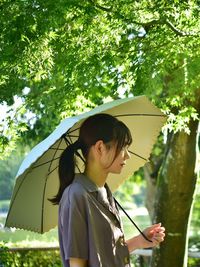 Woman holding umbrella while standing against trees