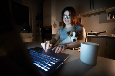 Smiling woman using laptop while sitting with dog at home