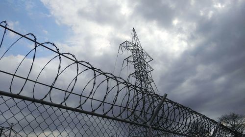 Low angle view of electricity pylon and railing against cloudy sky at dusk