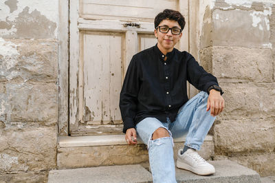 Young transgender man posing sitting on the front steps of a house.