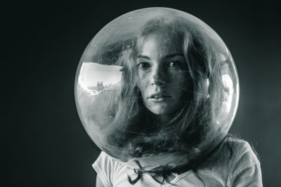 Young woman wearing glass container against black background