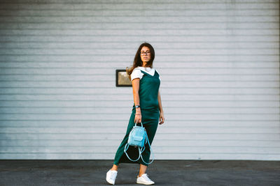 Full length of woman standing on footpath against wall