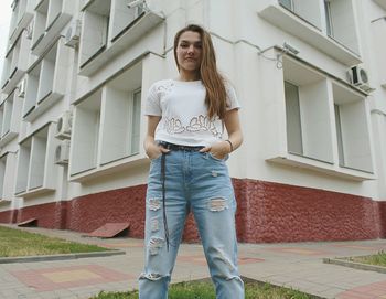 Portrait of young woman standing against building