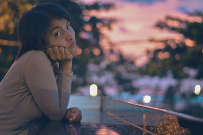 Portrait of young woman with hand on chin sitting outdoors