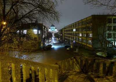 Illuminated street by buildings in city at night