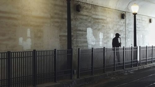 Rear view of man walking on illuminated wall by building