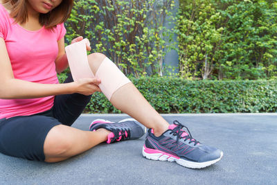 Low section of woman wrapping bandage on knee while sitting on footpath