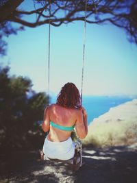 Rear view of young woman swinging at park against clear sky