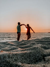 Full length of men on beach against sky during sunset