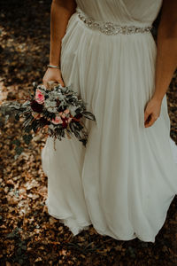 Low section of bride holding bouquet while standing on land