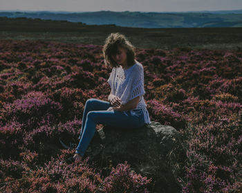 Young woman sitting on rock at field