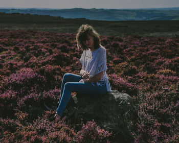 Young woman sitting on field against sky
