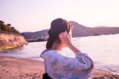 Rear view of young woman standing at beach against clear sky