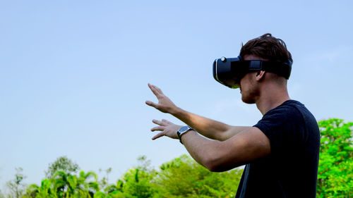 Man wearing virtual reality simulator against blue sky