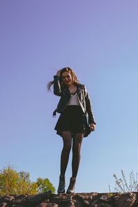 Full length of smiling young woman standing against clear blue sky