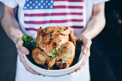 Midsection of man holding roasted chicken meat in bowl at home