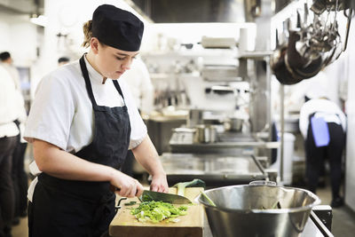 Young female chef chopping vegetables on cutting board in cooking school