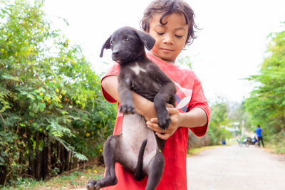 A girl in rural thailand, holding a dog along the road, teasing each other, dog, cute