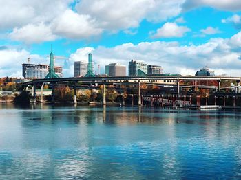 Bridge over river by buildings against sky