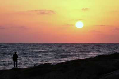 Silhouette man standing on beach against sky during sunset