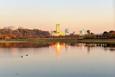 Reflection of buildings in lake against sky during sunset