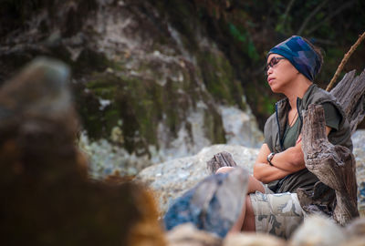 Young woman looking away while sitting on rock