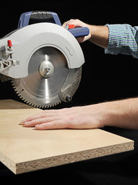 Cropped hand of man working with machinery against black background