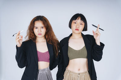 Portrait of lesbian couple holding pen standing against gray background