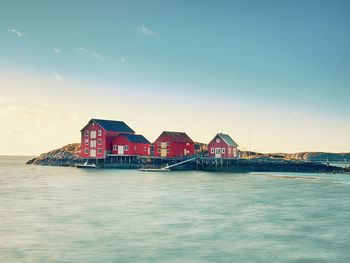 Stilt houses by sea against sky during sunset