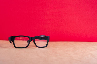 Close-up of eyeglasses on table against red background