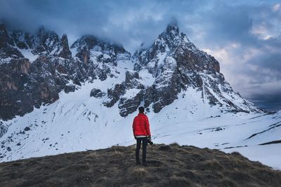 Rear view of man looking at snowcapped mountains against cloudy sky