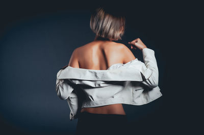 Rear view of seductive woman wearing jacket standing against black background