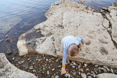 High angle view of boy reaching on rock against sea