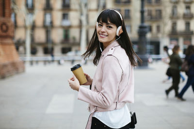 Spain, barcelona, smiling woman with coffee and headphones in the city