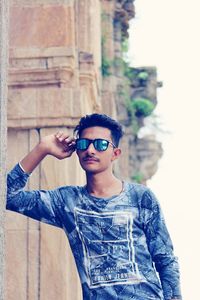 Portrait of young man wearing sunglasses standing against built structure