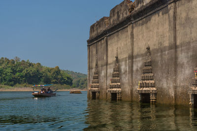 Boats sailing on river by buildings against clear sky