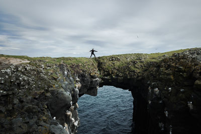 Man standing on rock by sea against sky