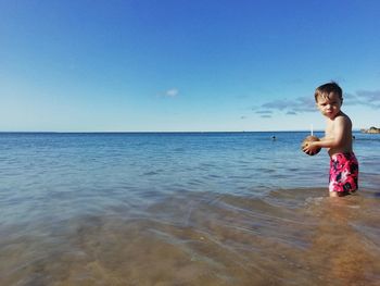 Full length of shirtless boy in sea against blue sky