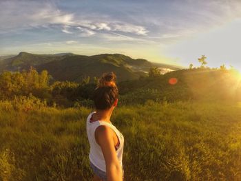 Side view of woman standing on grassy field against sky during sunset