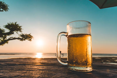 Beer glass on table against sea during sunset