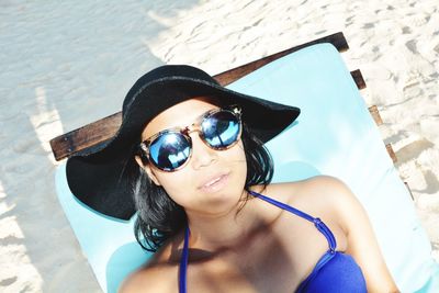 Young woman wearing sunglasses resting on lounge chair at beach