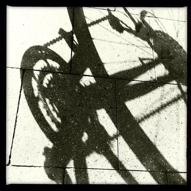 transfer print, shadow, auto post production filter, focus on shadow, sunlight, silhouette, bicycle, high angle view, day, outdoors, sidewalk, street, close-up, wall - building feature, no people, part of, outline, ground, transportation, unrecognizable person