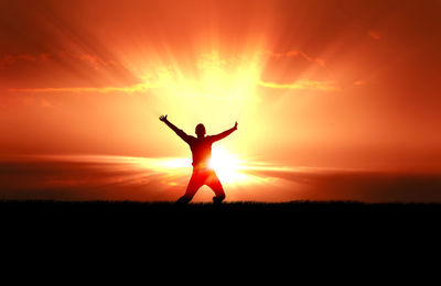 Silhouette man standing on field with arms raised against sky during sunset