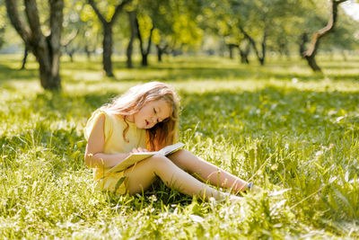 A little girl is sitting with a book in the garden. a girl reads a book on a summer day