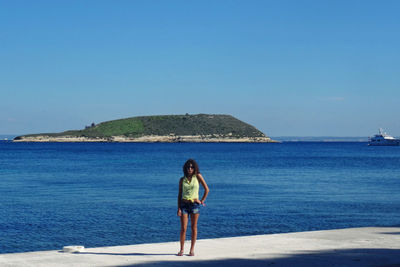 Woman standing on beach against clear blue sky