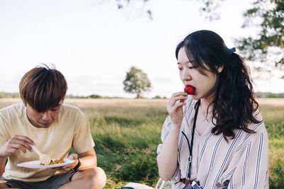 Woman eating strawberry while sitting with man at park during picnic