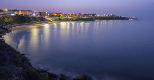 High angle view of illuminated city by sea against sky